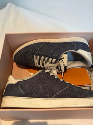 Äkta Louis Vuitton denim rivoli sneakers kommer med kvitto box och allt - Snygga sneakers från Louis Vuitton i mörkblå denim med vita detaljer och vita skosnören. Klassisk låg modell med stilren design och diskret LV-logga på sidan. Perfekta för dig som vill ha en exklusiv touch till din outfit.