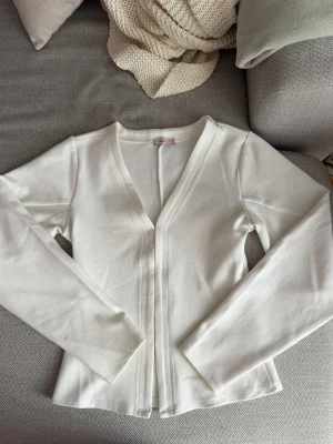 Vit långärmad topp från Nelly - Använd 1 gång. Säljer en stilren vit långärmad topp från Nelly. Toppen har v-ringning och är tillverkad i ett mjukt, stretchigt material som sitter snyggt på kroppen. Perfekt att matcha med jeans eller kjol för en clean look.