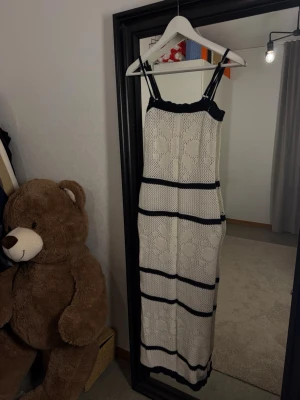 Vit och svart lång stickad klänning Ginatricot  - Supersnygg långklänning i vitt och svart med stickat blommönster och smala axelband. Klänningen har en rak passform och är perfekt för sommarens alla tillfällen. Materialet är mjukt och andas, vilket gör den bekväm att bära hela dagen. Aldrig använd utan prislapp M/S