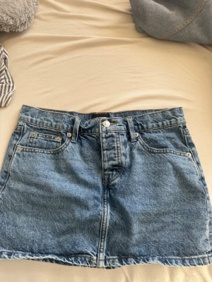 Blå jeanskjol med fickor - Säljer en klassisk blå jeanskjol i kort modell från lager 157.  Kjolen har en rak passform och perfekt att styla med en t-shirt eller hoodie för en avslappnad look. 