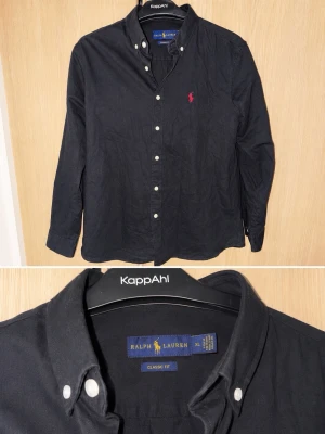 Svart skjorta från Ralph Lauren XL - Klassisk svart skjorta från Ralph Lauren i bomull med button-down krage och vita knappar. Skjortan har lång ärm och den ikoniska röda logotypen broderad på bröstet. Perfekt till jeans eller chinos för en stilren look.