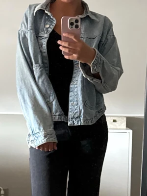 Ljusblå oversized jeansjacka - Trendig ljusblå jeansjacka i oversized modell med stora framfickor och klassisk krage. Jackan har knappstängning framtill och är tillverkad i denim. Perfekt att slänga över en hoodie eller t-shirt för en avslappnad look.