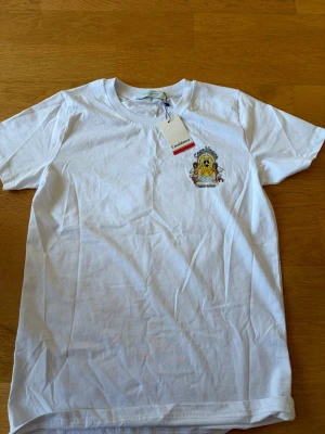 Vit t-shirt från Casablanca - Säljer en vit t-shirt från Casablanca med tryck på bröstet som visar två änglar, en sol och texten 'Sound'. T-shirten har rund hals och korta ärmar. Perfekt för dig som gillar stilrena plagg med coola detaljer.