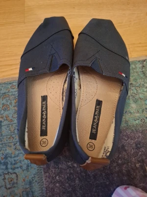 Mörkblå ballerinaskor Jean Paul - Snygga mörkblå ballerinaskor från Jean Paul i textilmaterial. Skorna har en spetsig tå, dekorativa sömmar och små broderade detaljer i rött, vitt och blått. Innersulan är ljus och vadderad för extra komfort.