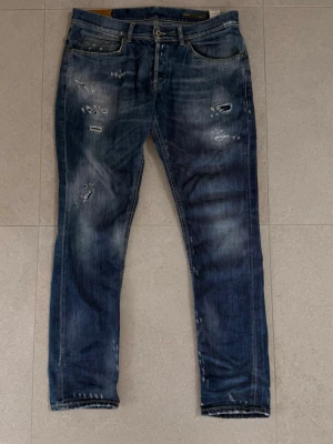 Blå slitna jeans med distressed detaljer - En snygg mörkblå tvätt från populära märket dondup. Dondup är ett väletablerat märke inom grischkulturen och söljs vanlitvis för 6-700kr på andrahandsmarknaden. Produkten har tydliga tecken på användning men har använts av mig i detta skick och de otiltänkta slitagen finns på tacksamma ställen och har inte påverkat upplevelsen.