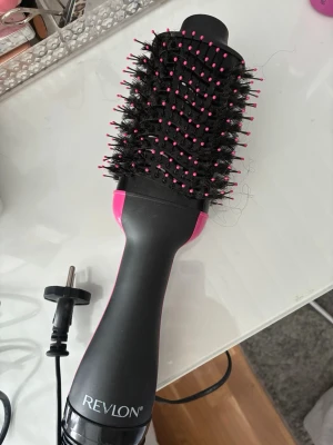 Revlon värmeborste  - En elektrisk varmluftsborste från Revlon i svart och rosa. Borsten har ovala borsthuvuden med täta borst och rosa piggar, perfekt för att styla och torka håret samtidigt. 