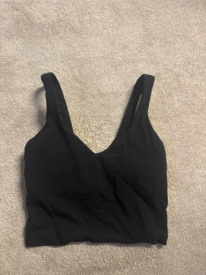 Svart tränings topp  från Lululemon - Snygg svart tränings topp  från Lululemon med breda axelband och djup urringning. Tillverkad i stretchigt och mjukt material som sitter skönt mot kroppen. Perfekt för dig som vill ha en enkel och stilren look.