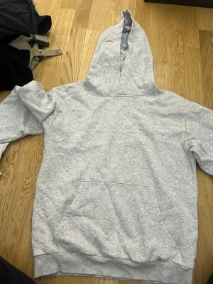 Ljusgrå hoodie från H&M - En basic ljusgrå hoodie från H&M med huva och magficka. Tillverkad i mjukt sweatshirtmaterial, perfekt för chill dagar. Klassisk passform och ribbade muddar vid ärmslut och nederkant. Enkel och stilren design som funkar till det mesta.