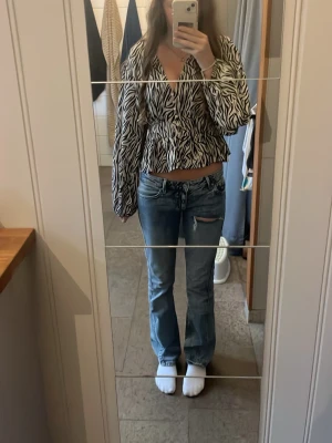 Blå bootcut jeans med slitning - Säljer ett par blå bootcut jeans med lätt slitning och hål vid ena låret. Jeansen har klassisk femficksmodell och normal midja. Perfekta för dig som gillar en avslappnad och trendig stil.