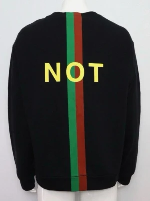 Svart Gucci hoodie med text och ränder - Svart hoodie från Gucci med gul texten 'NOT' på ryggen och en vertikal grön och röd rand som går från nacken till nederkanten. Tillverkad i mjuk bomull och har en avslappnad passform. Perfekt för dig som vill sticka ut med en unik design.