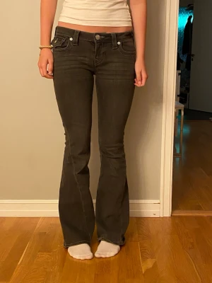 True religion jeans - Snygga mörkgrå bootcut jeans med dekorativa fickor bak och vita sömmar. Jeansen har låg midja och utsvängda ben, vilket ger en retro och trendig look. Perfekta för dig som gillar en avslappnad men ändå stilsäker stil. Storlek w26 från true religion, passar S/m men mest S. Aldrig använda 