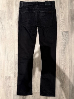 Nudie Jeans Grim Tim Svarta W32/L34 - Slim Straight Fit - Nudie Jeans Grim Tim ”Org. Black Ring” svarta jeans med slim straight fit-passform, normal midja och raka ben, storlek W32/L34, midja 40 cm, ytterbenslängd 105 cm, benöppning 17 cm, modellen är 185cm & väger 65kg, i fint skick.