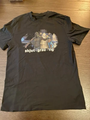 Svart t-shirt med tryck från 2002 Produktion - Svart t-shirt från 2002 Produktion med coolt tryck på bröstet och texten 'skjut · gräv · tig'. Klassisk passform och rund halsringning. Perfekt för dig som gillar unika motiv och streetwear-vibe.