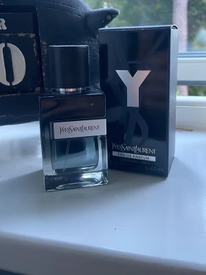 Yves Saint Laurent Y Eau de Parfum - Y Eau de Parfum från Yves Saint Laurent med stilren svart och transparent glasflaska. Doften kommer i originalkartong och flaskan har en modern, maskulin design med metallisk svart kork och tydlig Y-logga på förpackningen.