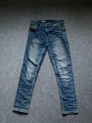 Blå skinny jeans med slitningar - Säljer ett par blå skinny jeans med snygga slitningar och tvättade detaljer. Jeansen har klassisk femficksmodell, normal midja och smal passform hela vägen ner. Materialet är denim med stretch för extra komfort.