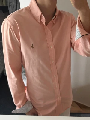 Ljusrosa skjorta från Ralph Lauren - Säljer en stilren och klassisk skjorta från Ralph Lauren. Perfekt för både vardag och mer uppklädda tillfällen.  Storlek: M Passform: Slim fit Färg: orange Skick: mycket bra  Skjortan är tillverkad i högkvalitativt material och har den ikoniska Ralph Lauren-loggan broderad på bröstet.  Hör av dig vid intresse eller frågor!
