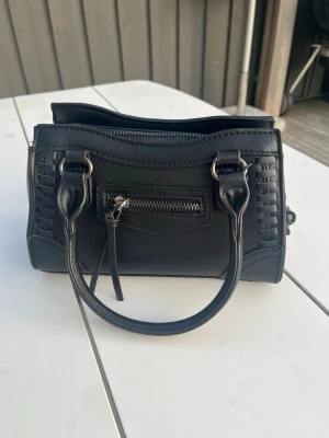 Svart liten handväska med detaljer - Snygg väska från Gina, säljer pga av att jag inte använder. Väskan går att ha utan axelremsband med det finns för den som vill ha det.