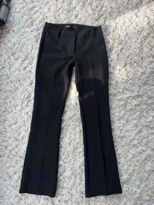 Svarta kostymbyxor med pressveck - Snygga svarta kostymbyxor med pressveck och raka ben. Byxorna har diskreta fickor bak och är tillverkade i ett slätt tyg som ger en stilren look. Perfekta för dig som vill ha en klassisk och enkel stil.