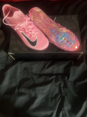 Nike rosa fotbollsskor Air Zoom - Säljer ett par grymma rosa Nike fotbollsskor med svart Swoosh och holografisk sula. Skorna har snörning och ovandel i mesh för bra ventilation. Sulan har coolt mönster och texten 'Air Zoom'. Perfekta för dig som vill sticka ut på planen.