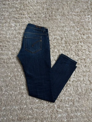 Mörkblå dondup jeans - Snygga mörkblå jeans med raka ben och klassisk femficksdesign. Jeansen har kontrastsömmar och en detalj på bakfickan. Materialet är denim i bomull med en skön känsla. Perfekta för dig som gillar en enkel men stilren look.
