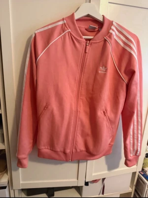 Rosa Adidas zip hoodie - Säljer en snygg rosa zip hoodie/jacka från Adidas. Trojan är köpt i New York 2019 och är aldrig använd. 