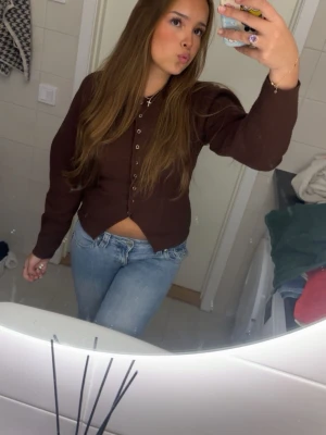 Brun ribbad kofta med knappar - Säljer en brun ribbad kofta med långa ärmar och knäppning framtill. Koftan har en figurnära passform och är tillverkad i ett mjukt, stretchigt material. Perfekt att styla med jeans eller mjukisbyxor för en chill look.