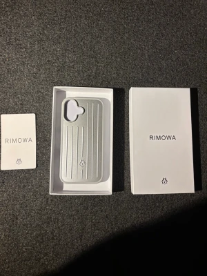 iPhone 16 Rimowa mobilskal - Snyggt och stilrent mobilskal i silver från Rimowa. Skalet har en räfflad design med vertikala linjer och en diskret logotyp längst ner. Tillverkat i ett hårt material som ger ett exklusivt intryck och skyddar mobilen på ett trendigt sätt.