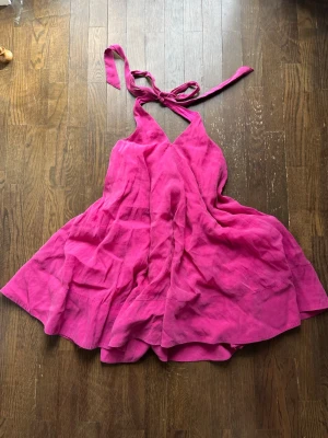 Rosa halterneck klänning  - Säljer en snygg rosa halterneck klänning med knyt i nacken och v-ringad hals. Klänningen har en luftig, volangig kjol och är ärmlös, perfekt för varma dagar. 