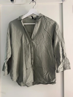 Ljusgrön blus med v-ringning - Snygg ljusgrön skjorta i linne med v-ringad hals och trekvartsärm. Skjortan har en avslappnad passform och knappar vid ärmsluten. Perfekt för dig som gillar en enkel men stilren look.