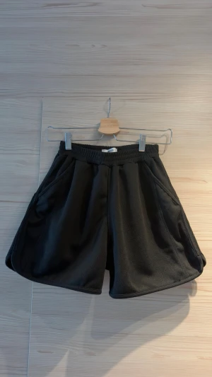Svarta loose shorts med resårmidja - Säljer ett par svarta shorts med loose passform och bred resår i midjan. Shortsen har sidofickor och är gjorda i ett mjukt, syntetiskt material. Köpta på klädbutiken WEGO i Japan, one size men skulle säga det är en S