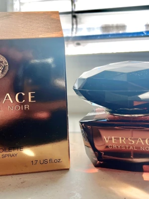 Versace Crystal Noir Eau de Toilette 50ml - Versace Crystal Noir Eau de Toilette i 50 ml flaska. Flaskan är mörklila med en exklusiv, diamantformad kork och gulddetaljer. Förpackningen är elegant i svart och guld med Versaces ikoniska logga. En lyxig och sofistikerad doft för dig som vill sticka ut.