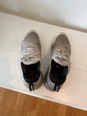 Nike Air Max 270 vita sneakers - Nike Air Max 270 sneakers i vitt med svarta detaljer och synlig luftdämpning i hälen. Ovandelen är i mesh för bra ventilation och har klassiska Nike-loggor på sidan och tån. Skorna har vita snören och svart insida för en clean look.
