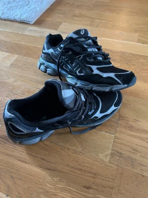 Svarta och grå Asics sneakers - Snygga Asics gel i svart och grått med coola detaljer och meshpaneler för bra ventilation. Skorna har en sportig look med robust sula och klassisk snörning. Perfekta för dig som gillar streetwear och vill ha bekväma skor till vardags.