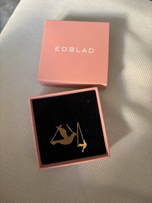 Guldhalsband från Edblad  - Snyggt och stilrent halsband i guld från Edblad med ett hänge i form av en duva. Kedjan är tunn och elegant, vilket gör att halsbandet känns lätt och smidigt att bära. Perfekt accessoar för dig som gillar minimalistisk design och fina detaljer.