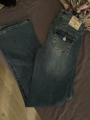 Blå bootcut jeans från True religon - Säljer ett par klassiska blå bootcut jeans från Becca i modellen Mid Rise Bootcut. Köpte dom i juli men har bara testat dom säljer dom pågrund dom inte kommer till användning går att diskutera priset. Köptes för 1399kr