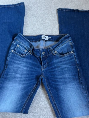 Blå bootcut jeans från 157 - Snygga blå bootcut jeans från 157 med klassisk femficksmodell och slitningar framtill. Jeansen har normalhög midja, dragkedja och knapp i silverfärg. Materialet är denim med en skön tvättad look och kontrastsömmar.