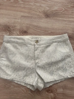 Vita broderade shorts med blommönster - Snygga vita shorts med diskret blommönster och broderad känsla. De har fickor både fram och bak samt stängs med knapp och dragkedja. Perfekta för sommarens alla tillfällen och ger en fräsch och elegant look.