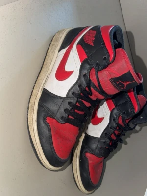 Svarta och röda jordan 1 - Säljer ett par jordan 1 i svart, rött och vitt med klassisk design och tydliga detaljer. Skorna har en röd swoosh på sidan, svart tåparti och röd plös med logga. Tillverkade i läder med vita paneler och svart snörning.