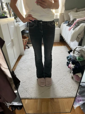 Svarta bootcut jeans med vita sömmar - Säljer ett par svarta bootcut jeans med tydliga vita kontrastsömmar. Jeansen har låg midja, klassiska fem fickor och utsvängda ben. Materialet är denim med stretch för extra komfort. Perfekta för en trendig och avslappnad look.