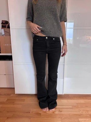 Svarta bootcut jeans med hög midja - Säljer ett par svarta bootcut jeans med hög midja och klassisk femficksmodell. Jeansen har en smal passform upptill och lätt utsvängda ben. Materialet är stretchigt denim som sitter snyggt och bekvämt. Perfekta till en avslappnad eller trendig look.
