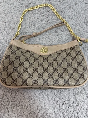 Beige GG canvas handväska  - Säljer en beige handväska i klassisk GG canvas med läderdetaljer och guldfärgad kedja. Väskan har ikoniskt GG-mönster och en elegant form som passar perfekt till din outfit. Levereras med original dustbag och box.