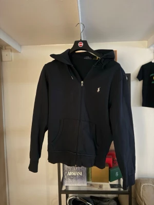 Svart hoodie från Polo Ralph Lauren - Säljer en mörkblå hoodie från Polo Ralph Lauren med dragkedja framtill och klassisk huva. Tröjan har fickor på magen och den ikoniska broderade loggan i vitt på bröstet. Perfekt för en avslappnad och stilren look. Köpt för 1950kr i Palma de mallorca i en ralph lauren butik för ca 1 år sedan. Den är äkta och är i storlek M.