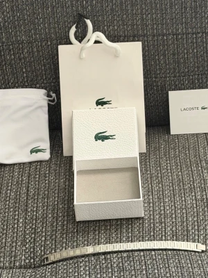Lacoste Bracelet - Lacoste armband, ungefär 21cm lång och går att förkorta precis som en klocka. Kommer med allt som finns i bilden