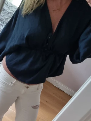 Marinblå blus med knappar - Snygg marinblå blus med v-ringning och knappar framtill. Blusen har en lös passform och långa ärmar, samt ett lätt glansigt material som ger en stilren look