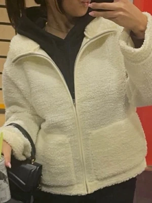 Vit teddyjacka med dragkedja - Mysig vit teddyjacka med hög krage och hel dragkedja framtill. Jackan har två stora fickor på framsidan och är tillverkad i fluffigt teddy-material som ger en cool och avslappnad look.