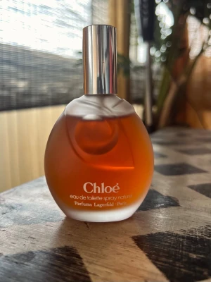 Chloé by Lagerfeld, 50ml, Vintage, discontinued  - Chloé eau de toilette spray från Parfums Lagerfeld Paris. Flaskan är rund med frostat glas och har en varm bärnstensfärgad vätska. Locket är silverfärgat och flaskan har en elegant, klassisk design som känns lyxig och tidlös.
