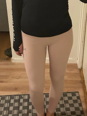 Ljusrosa ribbade leggings - Säljer ett par ljusrosa ribbade leggings med hög midja och tight passform. Materialet är stretchigt och bekvämt, perfekt för både träning och chill. Diskret logga på höften. Supersnygga att matcha med en oversized hoodie eller crop top.