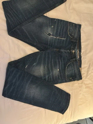 Blå slitna tom tailor jeans med slitningar  - Säljer ett par blå jeans med coola slitningar och distressed detaljer på både fram- och baksida. Jeansen har klassisk femficksmodell och är tillverkade i denim med en snygg tvättad look. Perfekta för en avslappnad och trendig stil.