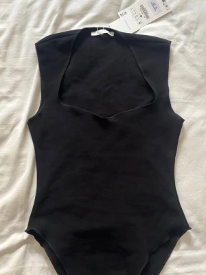 Svart ärmlös bodysuit med v-ringning - Sååå snygg svart bodysuit med ärmlös design. Perfekt att styla till jeans eller kjol för en trendig look. Tillverkad i mjukt material som sitter tight mot kroppen och framhäver figuren. Såå snygg att gå ut med men är tyvärr för liten på mig💕köpte på en Zara i Frankrike och har ej sett i svenska butiken så kan va slutsåld. Aldrig använd endast prövad