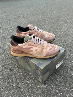 Unika, rosa Valentino rockrummers  - Säljer ett par snygga sneakers från Valentino med rosa och beige camomönster, detaljer i mocka och läder samt nitar vid hälen. Skorna har en beige sula och mörkbruna detaljer vid hälen. Kommer med originalkartong och dustbag.
